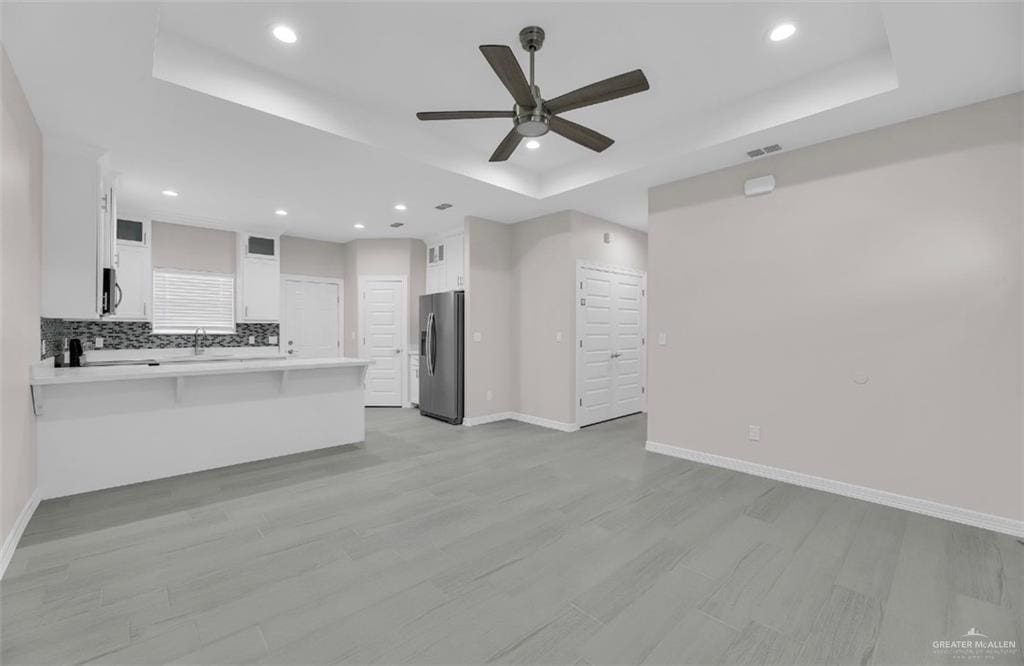 kitchen featuring kitchen peninsula, stainless steel appliances, white cabinetry, and a tray ceiling