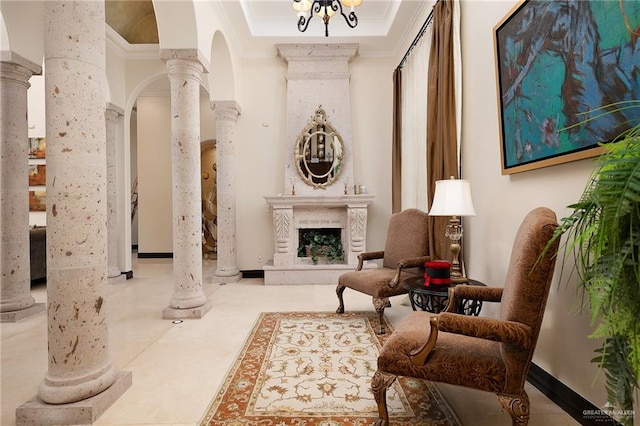 living area with an inviting chandelier, a raised ceiling, a premium fireplace, decorative columns, and crown molding