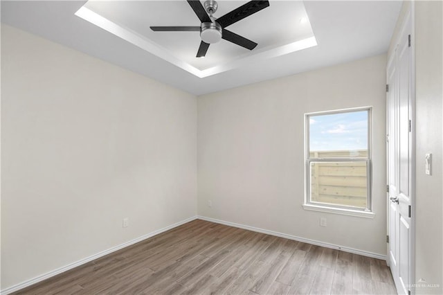 spare room featuring light hardwood / wood-style floors, ceiling fan, and a tray ceiling