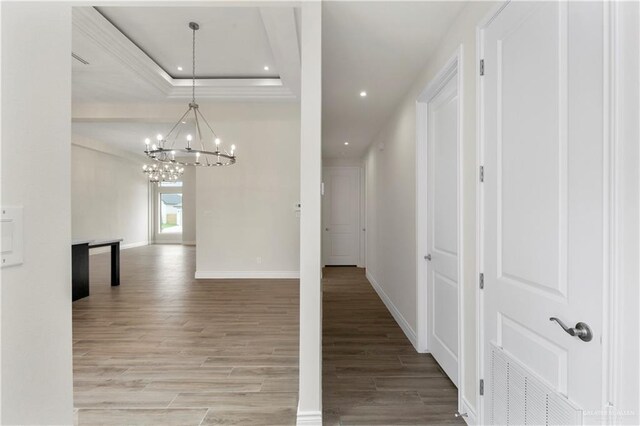 hallway featuring a raised ceiling, hardwood / wood-style floors, and an inviting chandelier