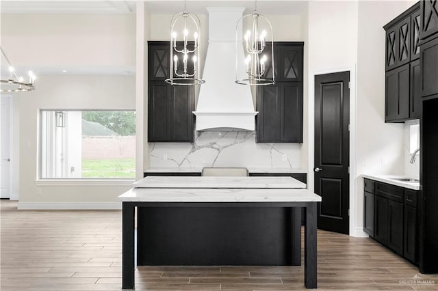 kitchen featuring tasteful backsplash, light hardwood / wood-style floors, decorative light fixtures, a kitchen island, and custom exhaust hood