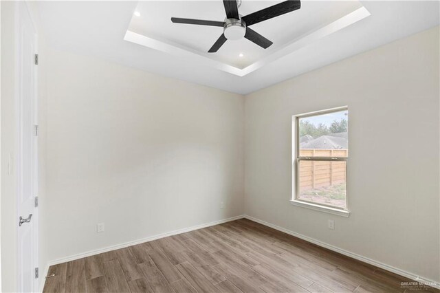 empty room featuring ceiling fan, light wood-type flooring, and a tray ceiling