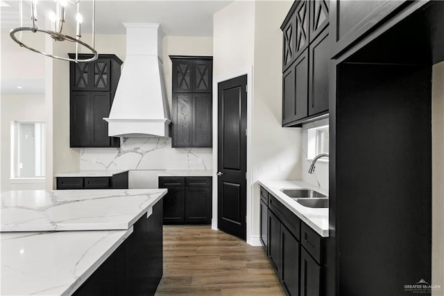 kitchen with light stone countertops, custom range hood, dark wood-type flooring, sink, and decorative light fixtures