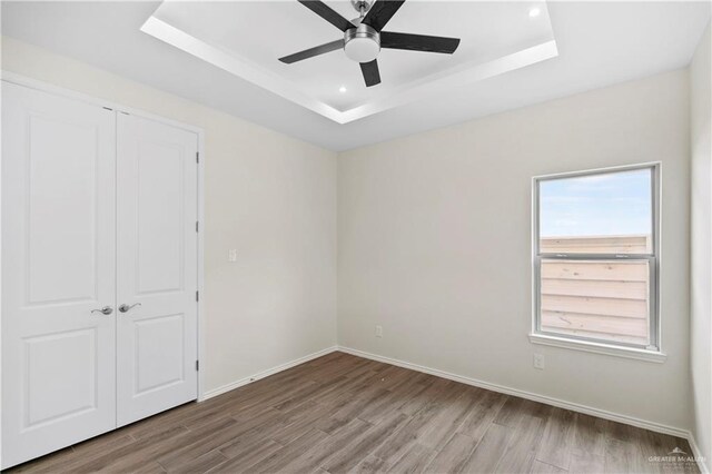 unfurnished bedroom featuring a closet, hardwood / wood-style flooring, ceiling fan, and a tray ceiling