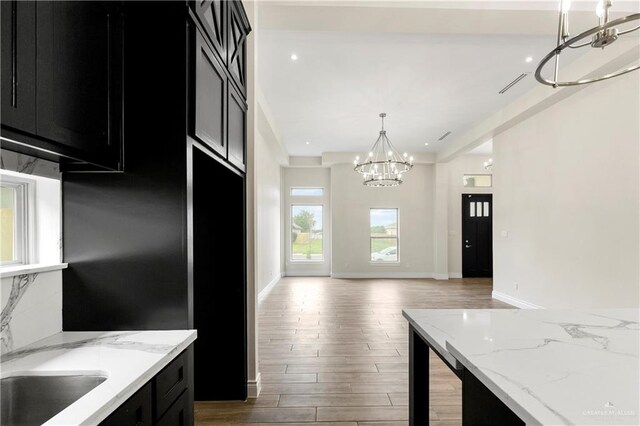 kitchen with light stone counters, decorative light fixtures, dark hardwood / wood-style floors, and an inviting chandelier