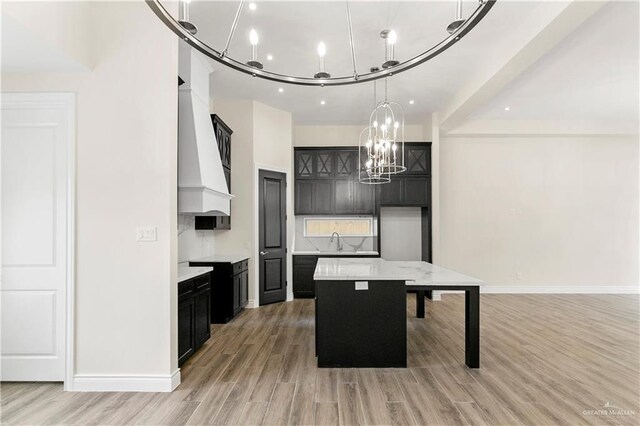 kitchen with premium range hood, an inviting chandelier, light hardwood / wood-style floors, a kitchen island, and hanging light fixtures