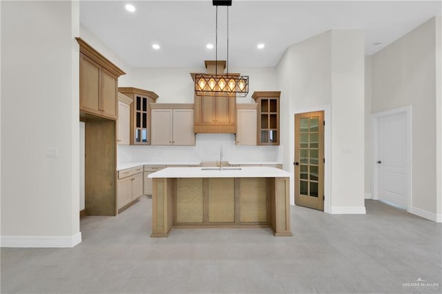 kitchen featuring glass insert cabinets, decorative light fixtures, a sink, light countertops, and a center island with sink