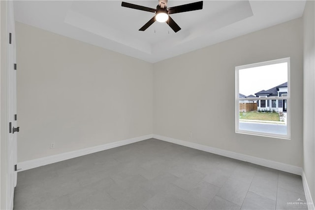 unfurnished room featuring ceiling fan, a raised ceiling, and baseboards