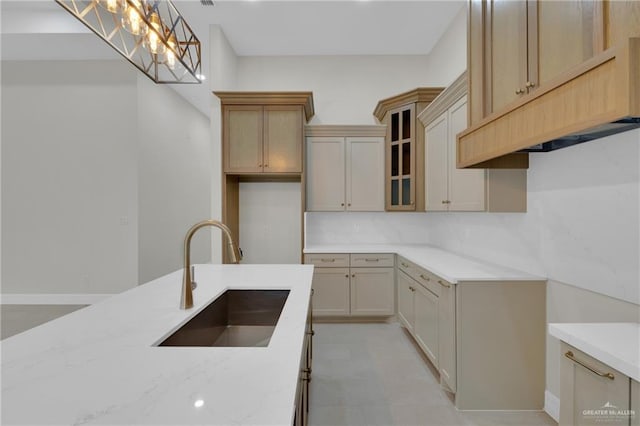 kitchen with a sink, hanging light fixtures, light brown cabinetry, tasteful backsplash, and glass insert cabinets