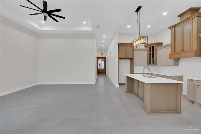 kitchen with light countertops, hanging light fixtures, glass insert cabinets, a kitchen island with sink, and a sink