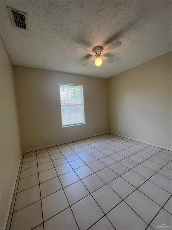 empty room with ceiling fan, light tile patterned floors, and a textured ceiling