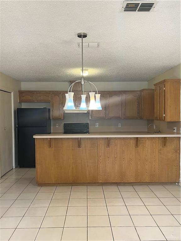 kitchen featuring pendant lighting, black fridge, kitchen peninsula, and a textured ceiling