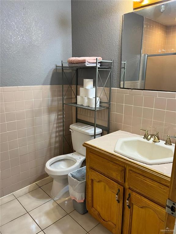 bathroom with an enclosed shower, vanity, tile walls, tile patterned flooring, and toilet