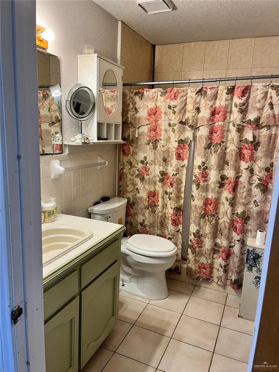 bathroom with vanity, a textured ceiling, tile walls, tile patterned flooring, and toilet