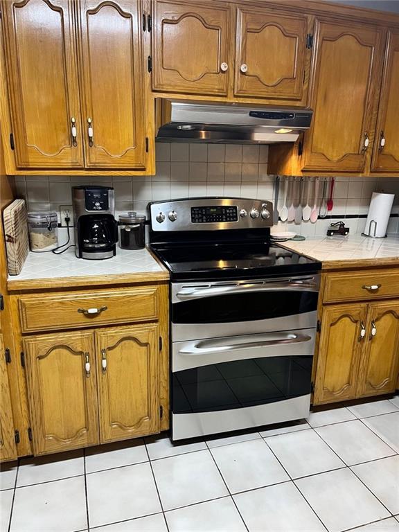 kitchen with stainless steel electric range, light tile patterned flooring, and tasteful backsplash