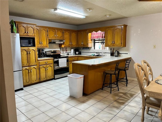 kitchen featuring decorative backsplash, light tile patterned flooring, a kitchen bar, kitchen peninsula, and stainless steel appliances