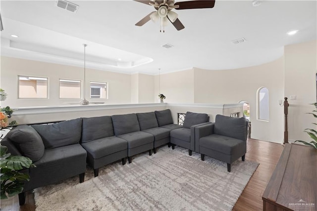 living room with hardwood / wood-style floors, a raised ceiling, and ceiling fan