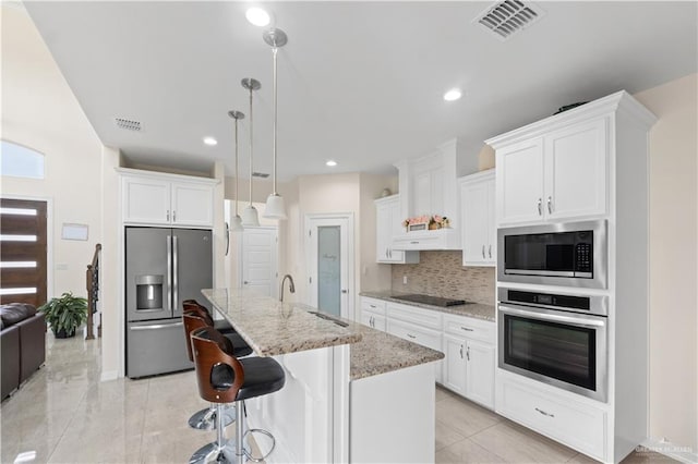 kitchen with appliances with stainless steel finishes, decorative light fixtures, white cabinetry, an island with sink, and sink