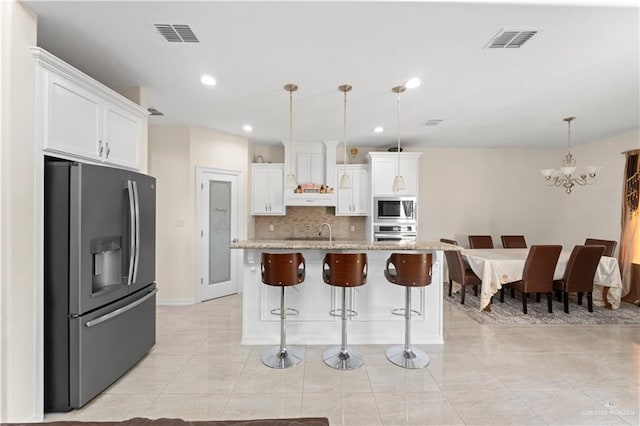 kitchen with appliances with stainless steel finishes, pendant lighting, white cabinets, a kitchen island with sink, and light stone counters