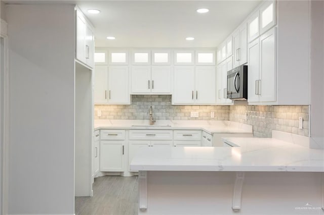 kitchen with white cabinetry, sink, light stone countertops, and kitchen peninsula