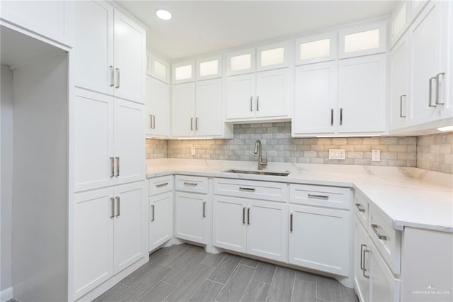 kitchen with backsplash, light stone countertops, sink, and white cabinets