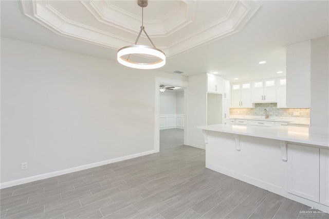 kitchen with white cabinetry, a tray ceiling, kitchen peninsula, and pendant lighting