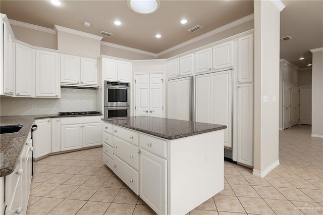 kitchen with a kitchen island, white cabinetry, stainless steel appliances, and dark stone counters