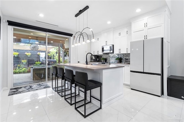 2215 Corales St, Mission, TX 78573 - kitchen featuring freestanding refrigerator, stainless steel microwave, a breakfast bar area, a center island with sink, and decorative backsplash