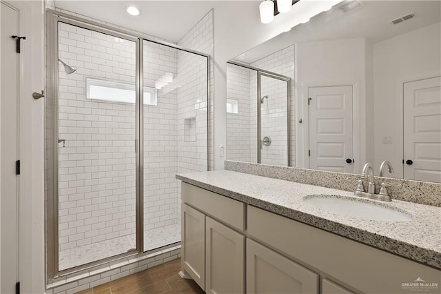 full bathroom with vanity, wood finished floors, a shower stall, and visible vents