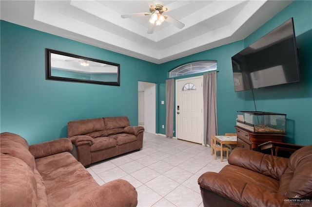 living room featuring a tray ceiling, ceiling fan, and light tile patterned floors