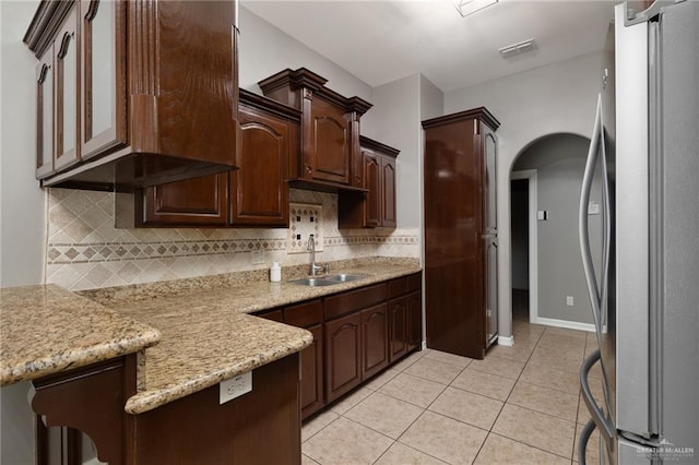 kitchen featuring light tile patterned flooring, arched walkways, freestanding refrigerator, a sink, and decorative backsplash