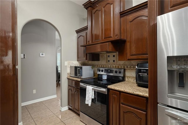 kitchen featuring backsplash, premium range hood, light tile patterned flooring, arched walkways, and stainless steel appliances