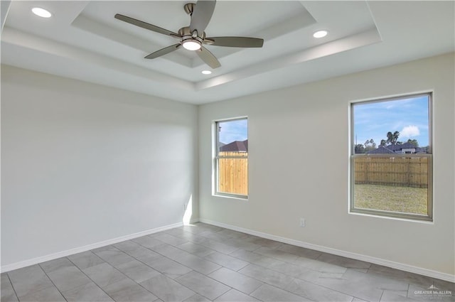 empty room featuring a tray ceiling, a wealth of natural light, and ceiling fan