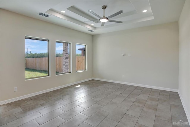 empty room with a tray ceiling, a wealth of natural light, and ceiling fan