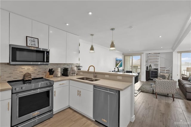kitchen with a sink, open floor plan, stainless steel appliances, a peninsula, and white cabinetry