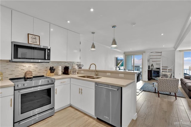 kitchen featuring light wood finished floors, stainless steel appliances, a sink, a peninsula, and open floor plan