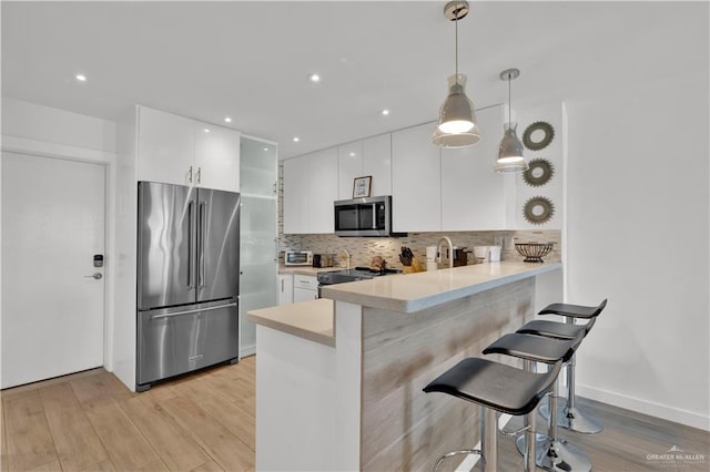 kitchen featuring white cabinets, a peninsula, light wood-type flooring, and appliances with stainless steel finishes