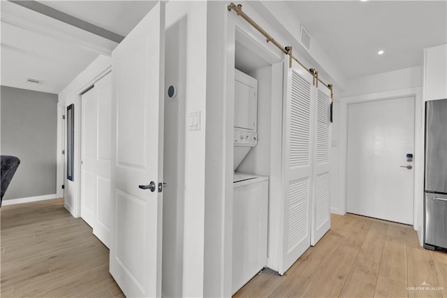 corridor with light wood finished floors, visible vents, stacked washer / dryer, and a barn door