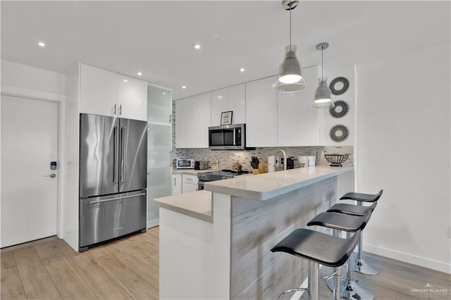 kitchen with white cabinets, light countertops, light wood-type flooring, a peninsula, and appliances with stainless steel finishes