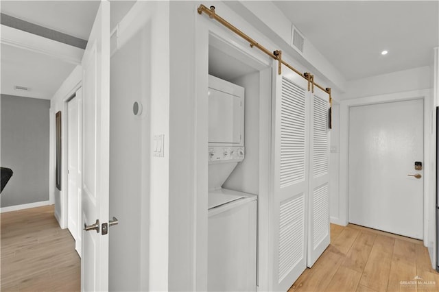 laundry room featuring light wood finished floors, stacked washer and dryer, a barn door, visible vents, and laundry area