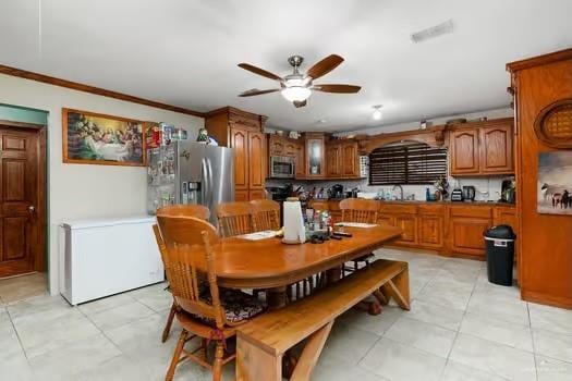 dining area featuring ceiling fan, sink, light tile patterned floors, and ornamental molding