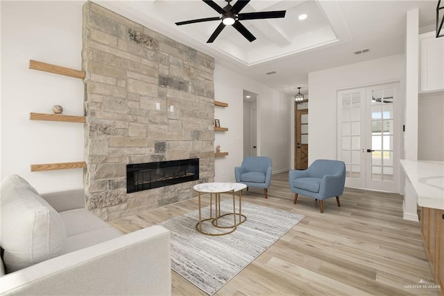 living room with ceiling fan, a stone fireplace, light wood-type flooring, and french doors