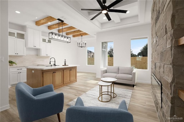 living room featuring sink, beamed ceiling, ceiling fan with notable chandelier, and light wood-type flooring