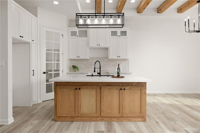 kitchen featuring pendant lighting, a center island with sink, light wood-type flooring, beam ceiling, and white cabinetry