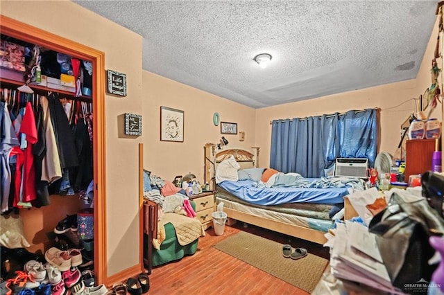 bedroom with hardwood / wood-style flooring, cooling unit, and a textured ceiling