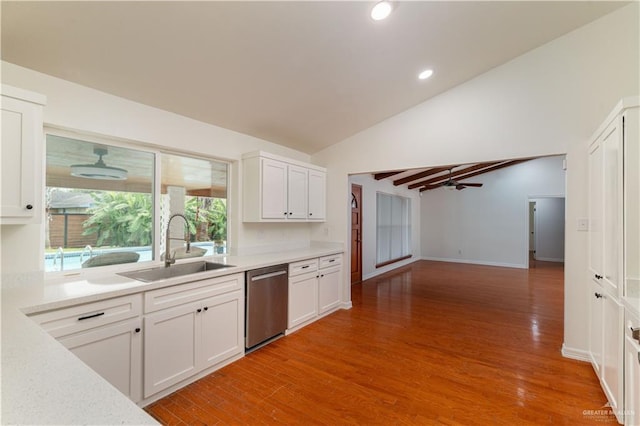 kitchen featuring stainless steel dishwasher, a sink, vaulted ceiling, light countertops, and white cabinets