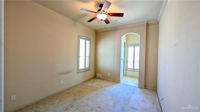 spare room with visible vents, arched walkways, light colored carpet, ceiling fan, and crown molding