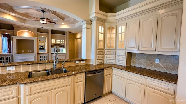 kitchen featuring dark stone counters, stainless steel dishwasher, a sink, and decorative columns