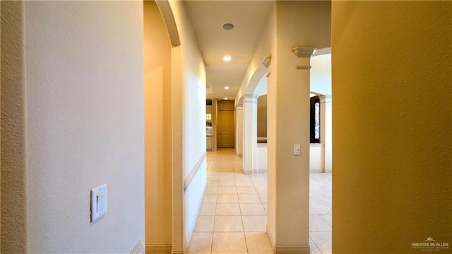 corridor with arched walkways, a textured wall, light tile patterned floors, recessed lighting, and ornate columns