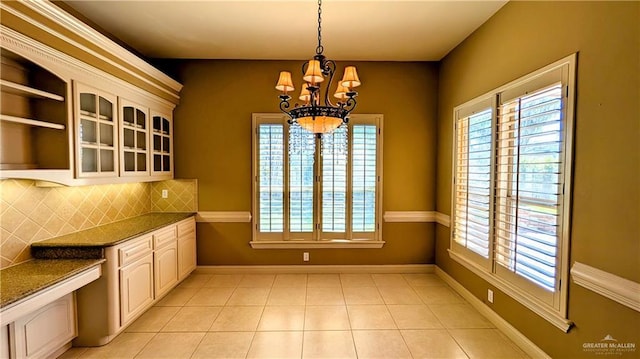 unfurnished dining area featuring light tile patterned floors, baseboards, and a notable chandelier